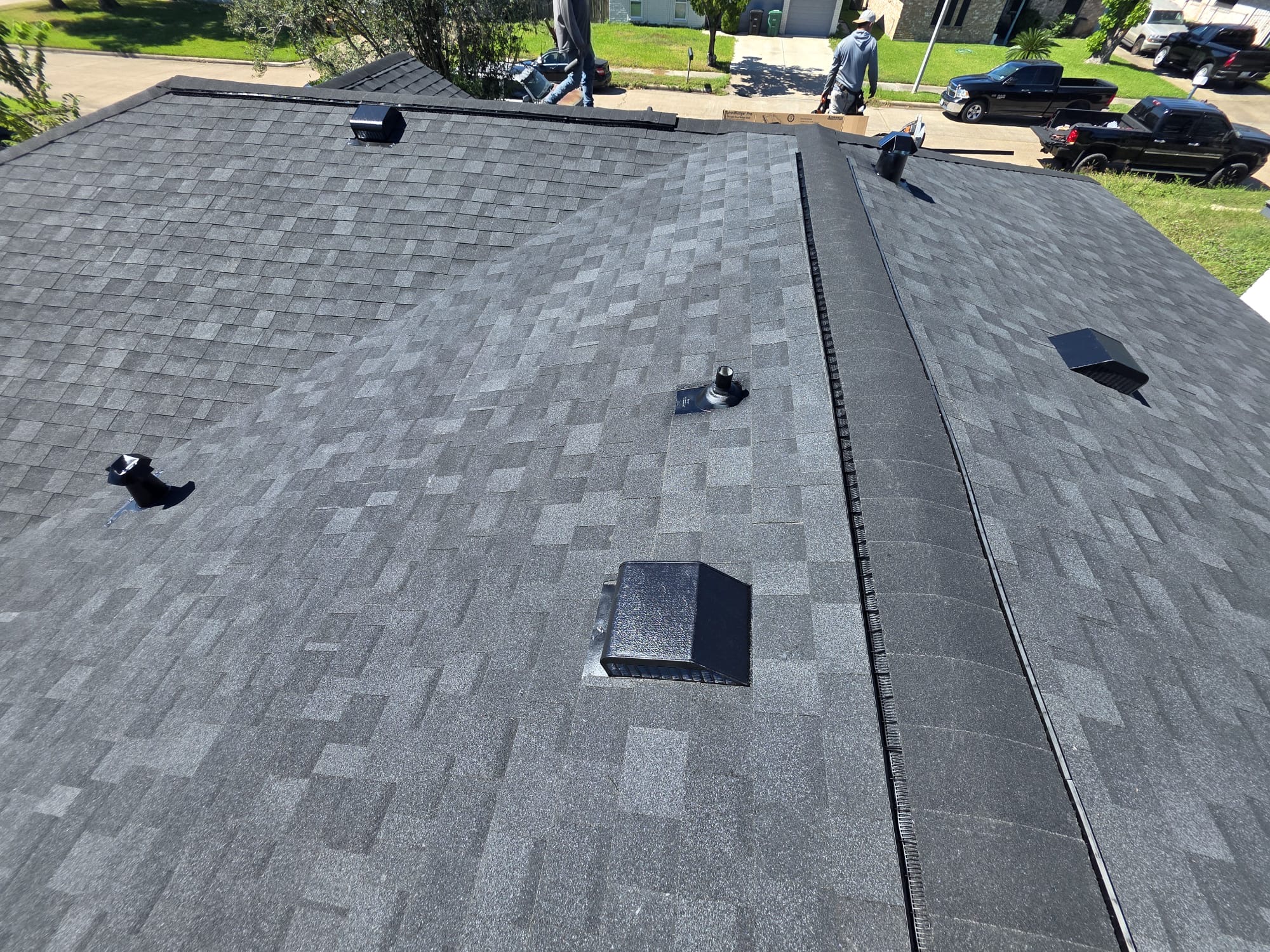 Newly installed dark architectural shingles with ridge vent and fresh pipe boots after replacement