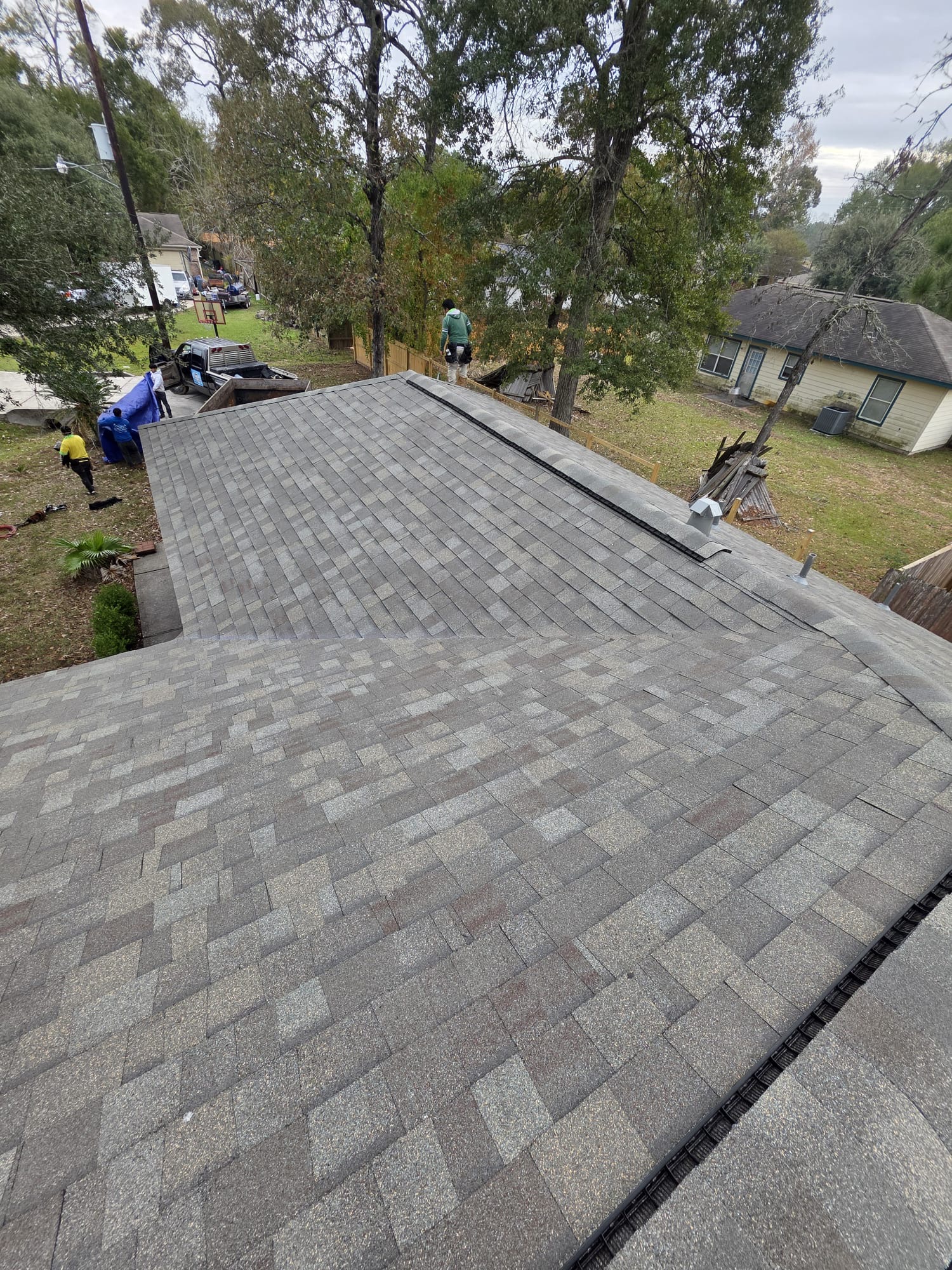 Newly installed multi-tone gray architectural shingles with ridge vent, with the crew working on and below the roof